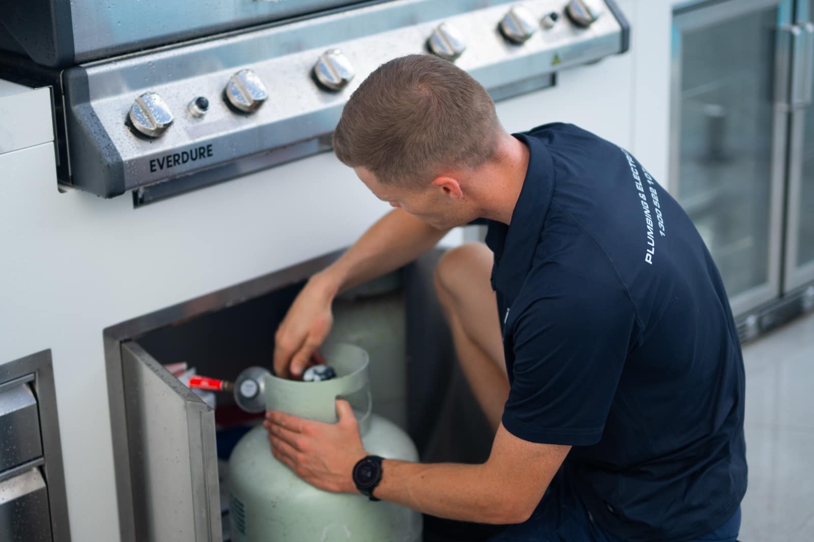 A Moral Service plumber changing over the gas bottle behind an outdoor kitchen on the Gold Coast