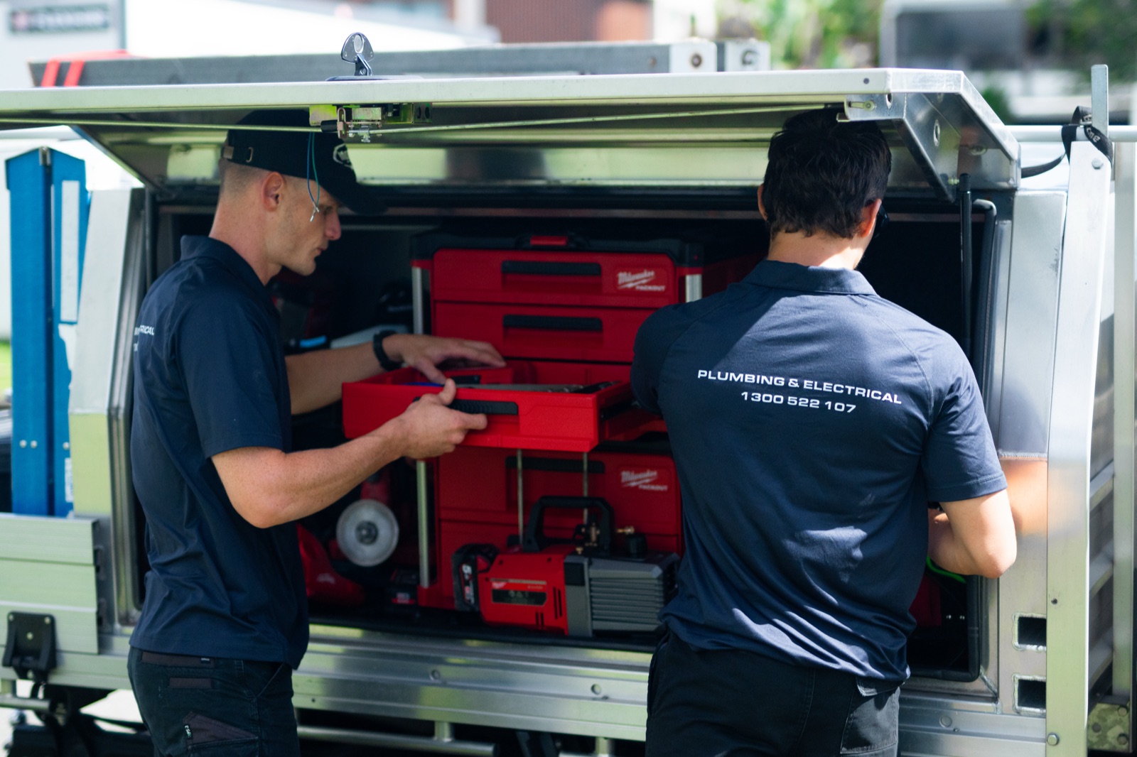 Two Moral Service tradesmen pulling tools from the back of the work ute, 1300 522 107 printed on the uniform