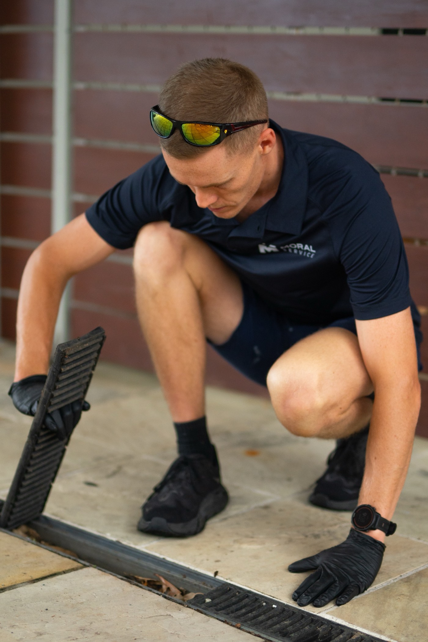 A Moral Service plumber lifting a drainage grate during a maintenance check